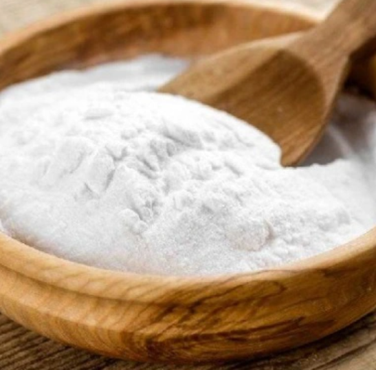 wooden bowl with wooden spoon partially submerged in a white flour like powder called Xanthan gum